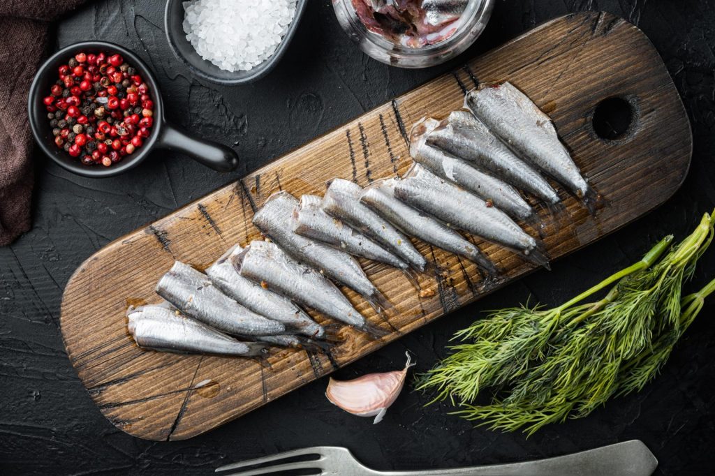 Pickled Anchovy set, on wooden cutting board, on black background with herbs and ingredients, top view flat lay Pickled Anchovy set, on wooden cutting board, on black background with herbs and ingredients, top view flat lay
