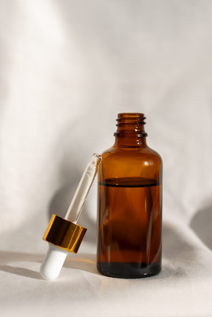 close-up-skin-regeneration-products Amber glass serum bottle with a gold dropper on white fabric, representing the skincare side of beauty.